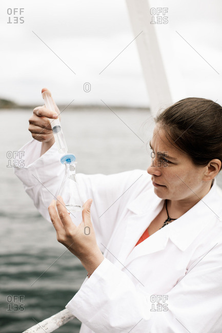 Female scientist injecting water in flask on boat in sea