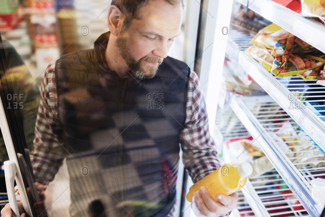 High angle view of male customer reading drink label at refrigerated section