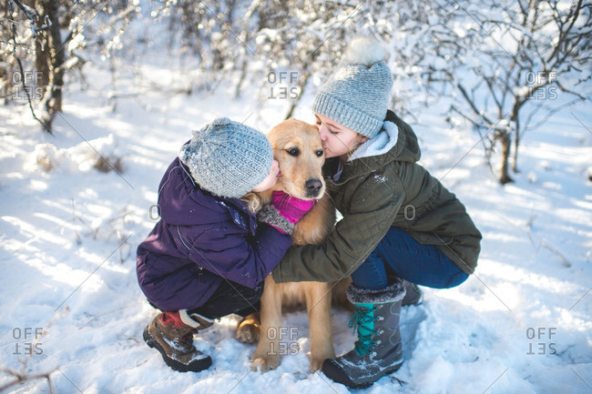 Two young girls, hugging dog, in th snow