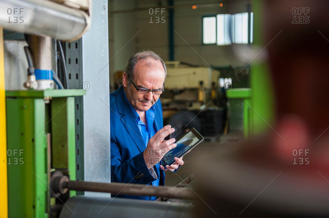 Man in manufacturing plant holding digital tablet examining component