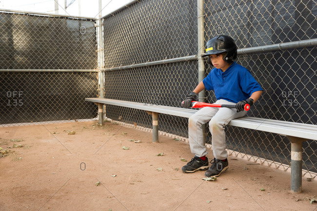 Boy with baseball sitting on bench at baseball practice
