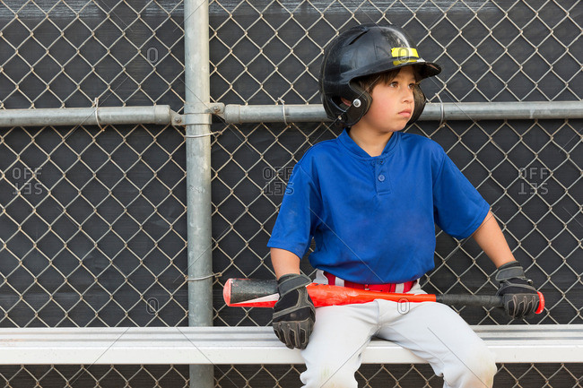 Boy with baseball bat watching from bench at baseball practice