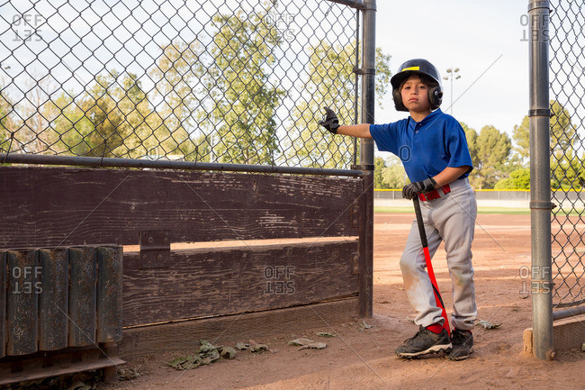 Portrait of boy with baseball bat leaning against fence at baseball practice