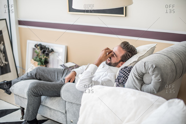 Young businessman reclining and laughing on hotel room chaise longue