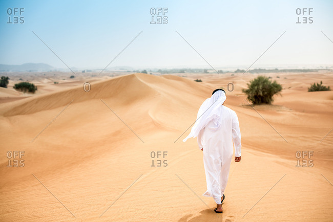 Rear view of middle eastern man wearing traditional clothes walking in desert