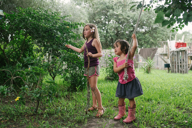 Sisters standing in a backyard playing with a stick and rope swing