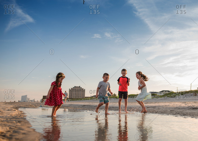 Four kids splashing in coastal puddle