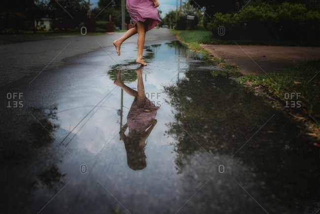 Girl tiptoeing on wet pavement reflected in a puddle