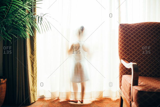 Girl standing behind sheer curtains by a bright window