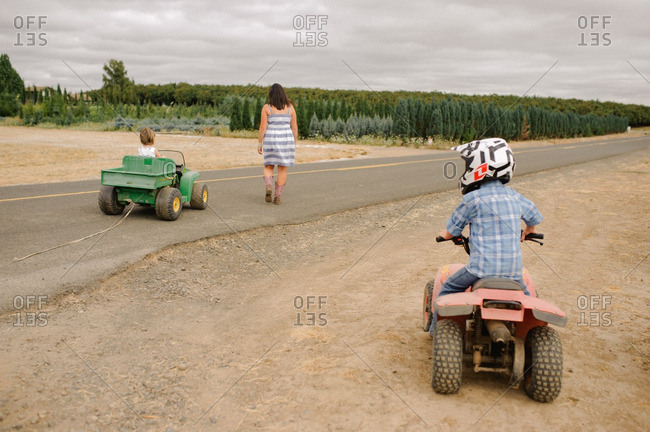 Boy on quad and girl in toy vehicle follow their mother on road