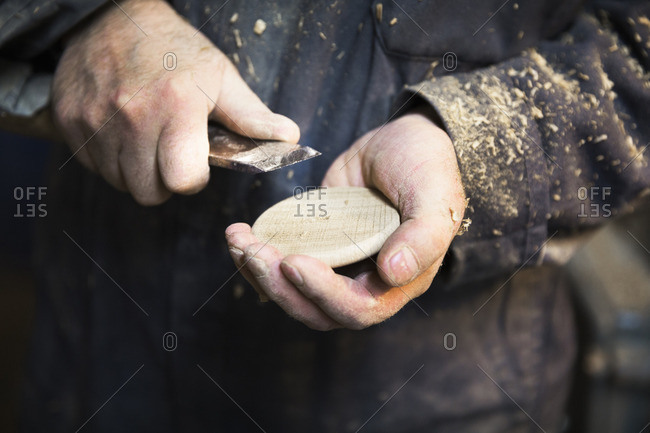 Close up of a man in a carpentry workshop, holding a wooden disk and a chisel in his hands