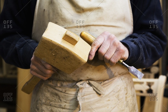 Close up of a man in a carpentry workshop, holding a wooden mallet and chisel