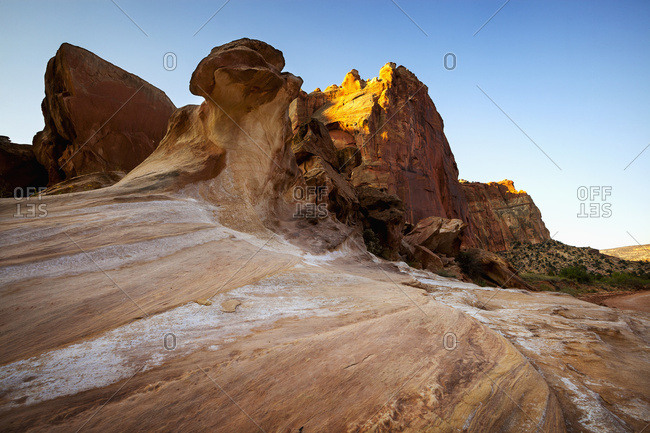 Rock formations in the foreground sweeping up to tall canyon cliffs in the background under clear blue skies, Capitol Reef National Park