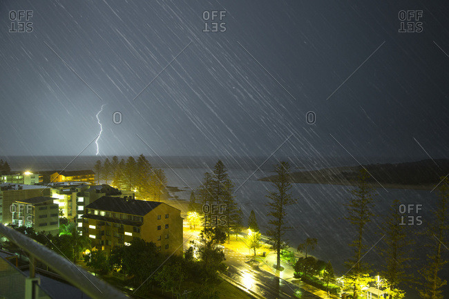 A lightning strike hits the ground in the distance and streaks of rain falling