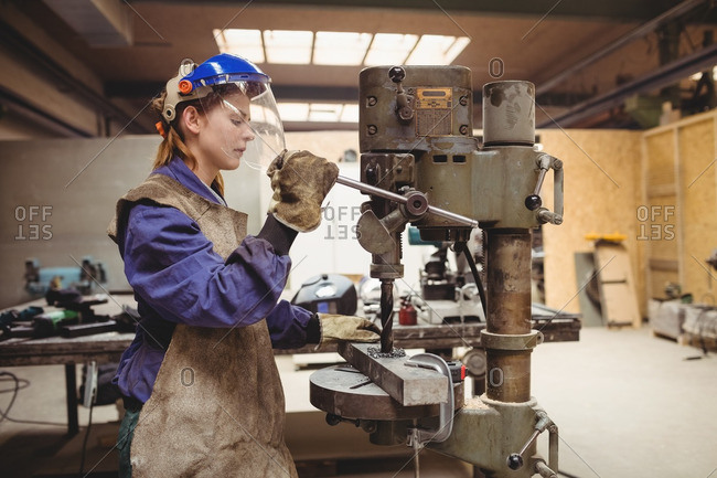 Female welder using a drill press in a workshop