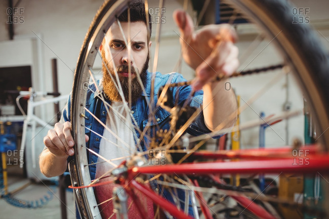 Portrait of a hipster repairing a bicycle wheel in a workshop