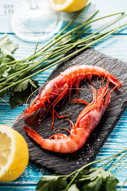 Elevated view of two fresh prawns on slate with lemon and parsley