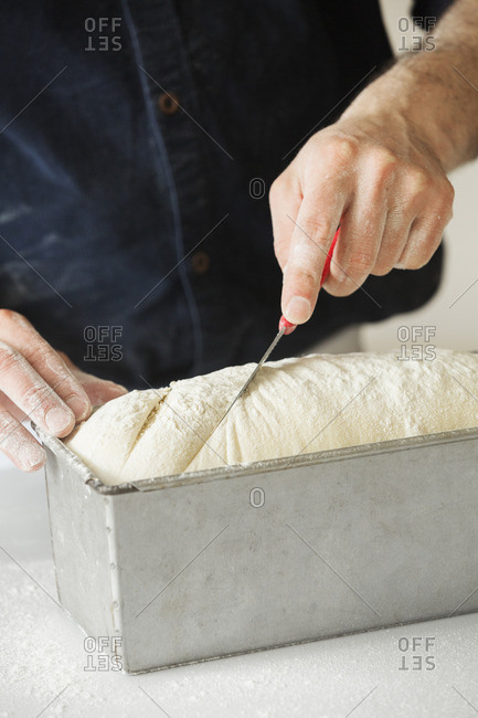 Close up of a baker cutting bread dough in a baking tin