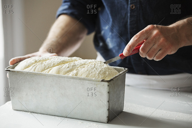 Close up of a baker cutting bread dough in a baking tin