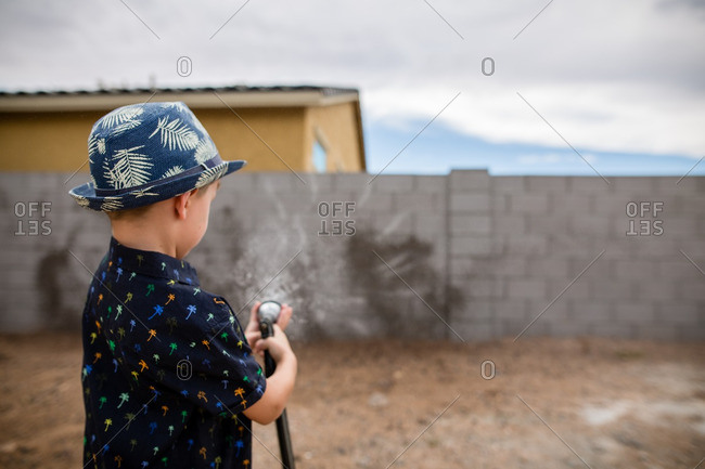 Boy spraying hose water at cement brick wall