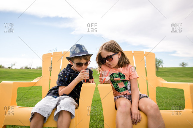 Siblings sitting on yellow chairs drinking icy drinks