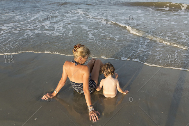 Mother sitting with naked toddler on the ocean shore