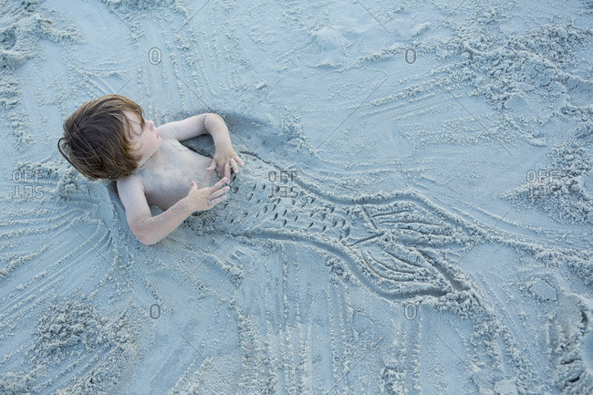 Boy buried in the sand with mermaid fin drawing