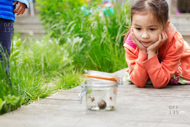 Young girl in garden watching jar of snails