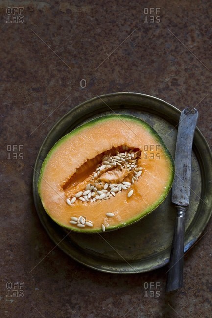 A halved cantaloupe melon on a pewter plate with an antique knife