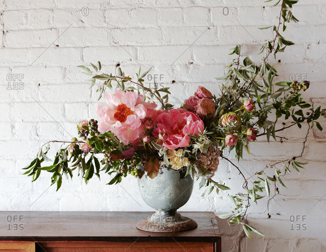 Floral arrangement made up of peonies in a vase on a wood bureau