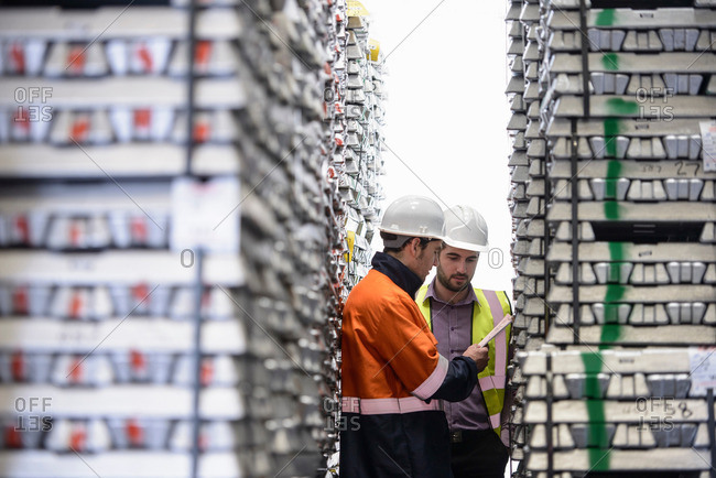 Workers inspecting stacks of aluminum ingots in warehouse
