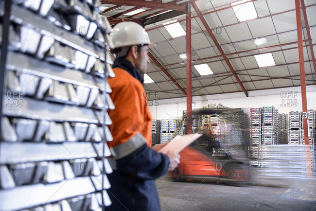 Worker watching forklift truck carrying aluminum ingots in warehouse, blurred motion