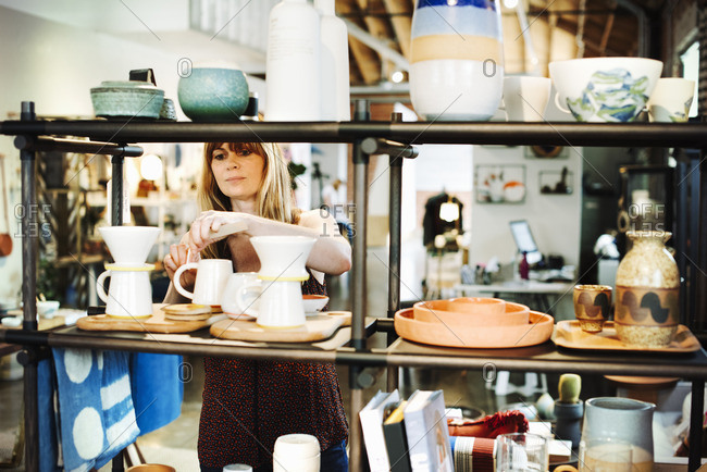Woman standing in a shop, arranging ceramic objects on a shelf