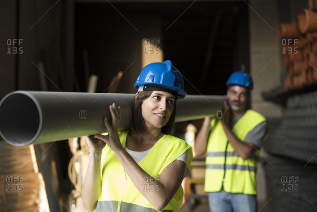 Construction workers carrying pipe in warehouse