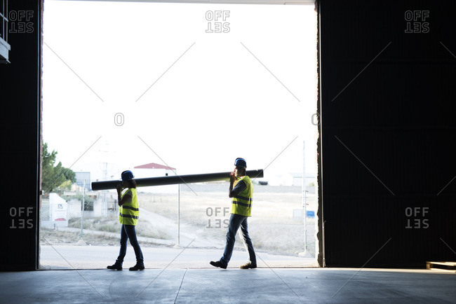 Construction workers carrying pipe in warehouse