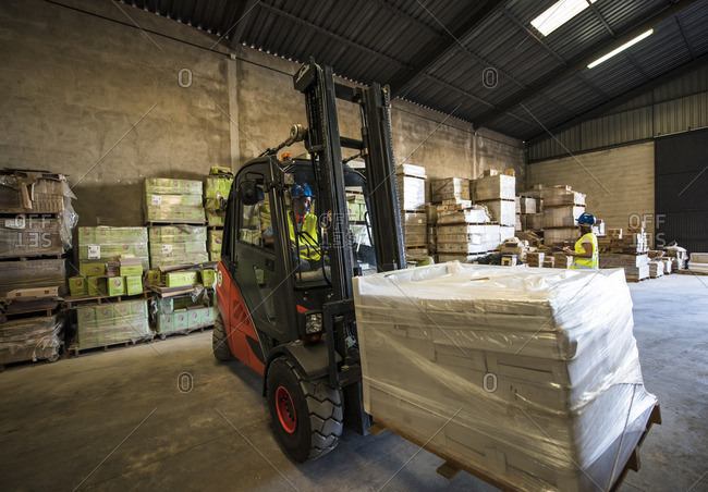 Workers transporting building material with forklift in warehouse