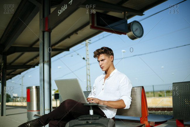 Young man using a laptop at station platform