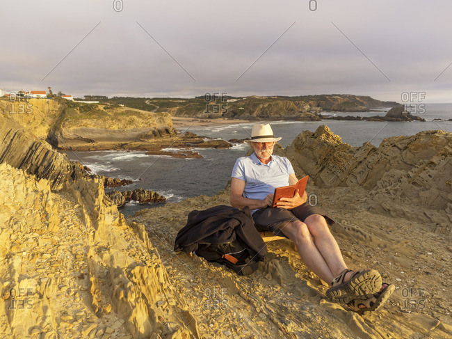 Portugal- Senior man sitting at beach- reading book