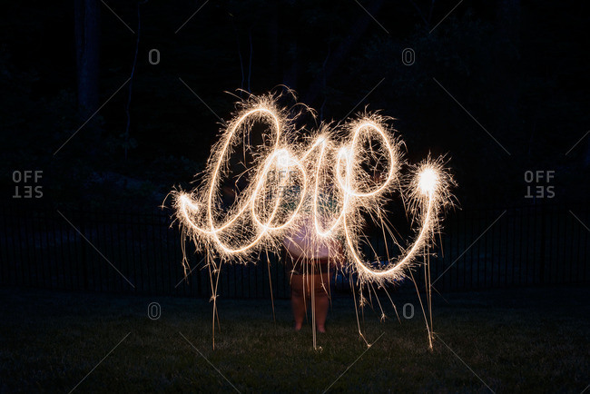 Person standing outside at night writing the word \'Love\' with a lit sparkler