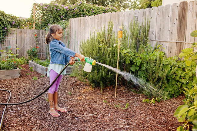 Side view of girl watering plants at backyard