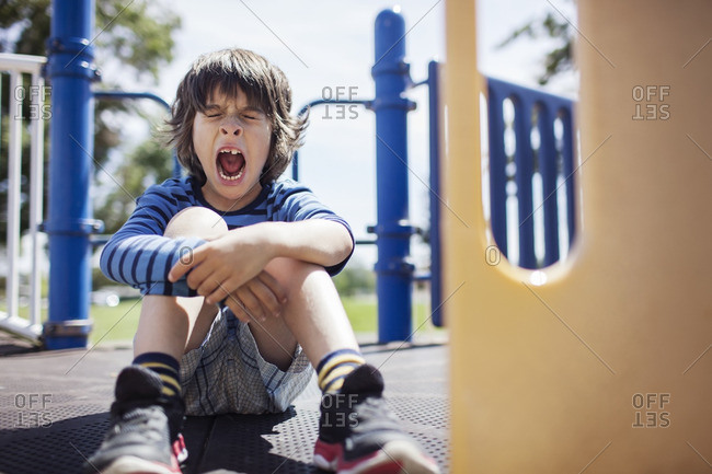 Boy yawning while sitting on outdoor play equipment