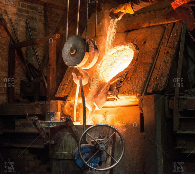 Worker adding flux to molten metal in foundry