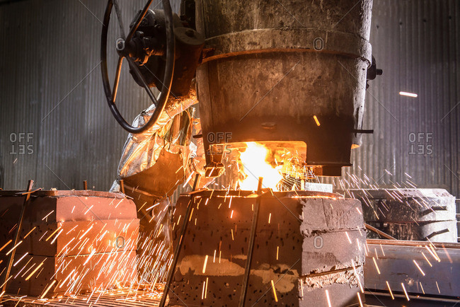 Worker pouring molten metal into molds in foundry