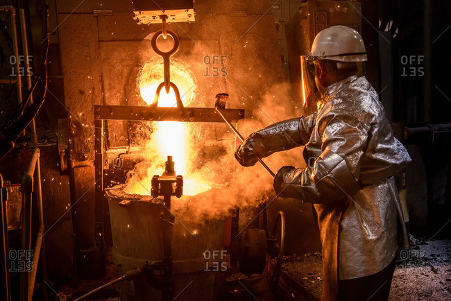 Worker pouring molten metal in foundry, rear view