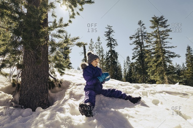 Girl sitting down on a snow covered hill making a snowball