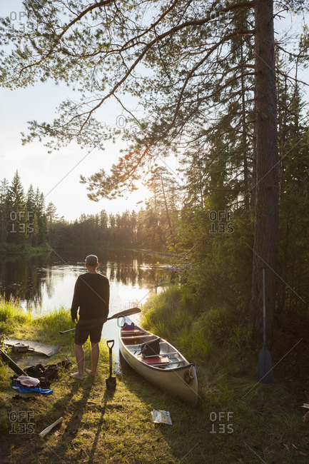 Sweden, Vastmanland, Svartalven, Man by canoe on riverbank