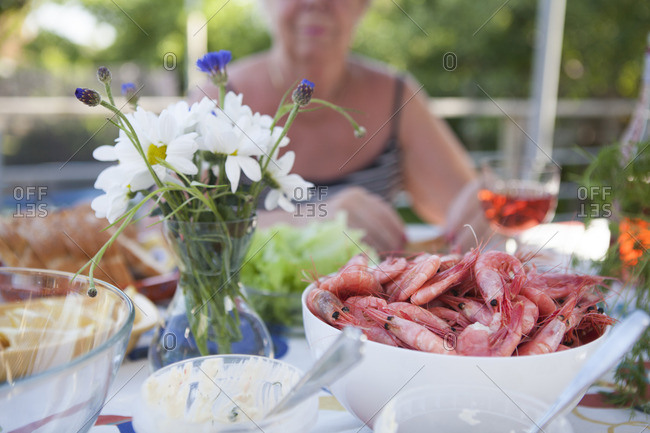 Sweden, Vastergotland, Lerum, Bowl of shrimps and flower vase on table, woman sitting in background