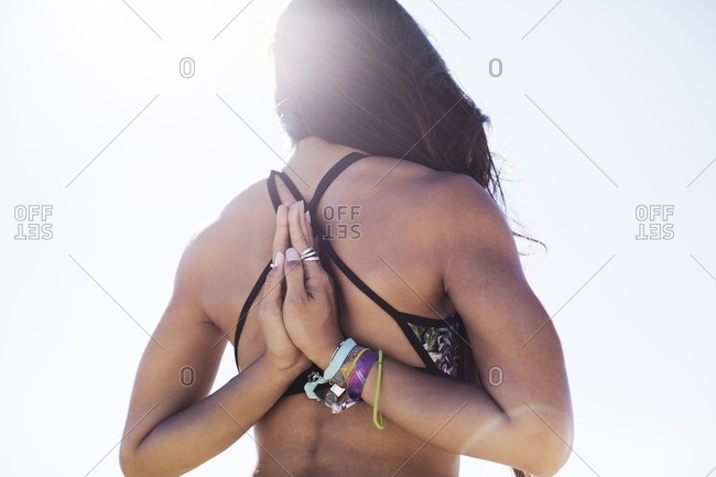 Rear view of young woman doing reverse prayer pose against clear sky on sunny day