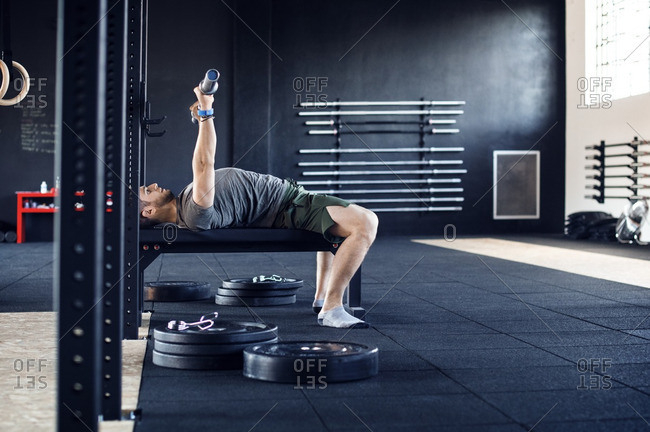 Side view of man lifting weight bar while lying on table in gym
