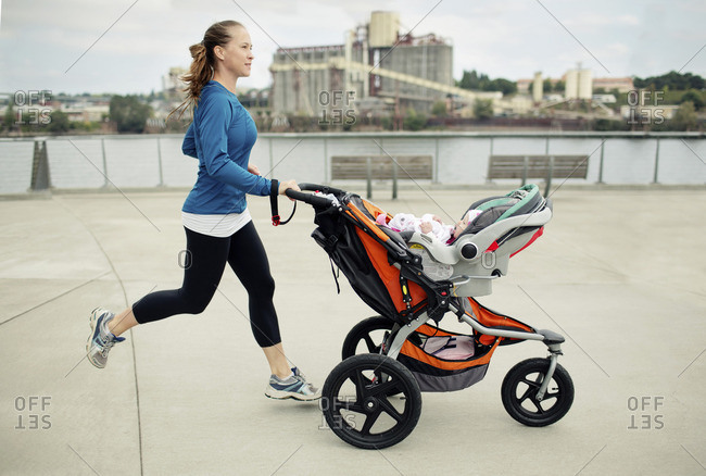 Side view of woman pushing baby stroller while jogging in city